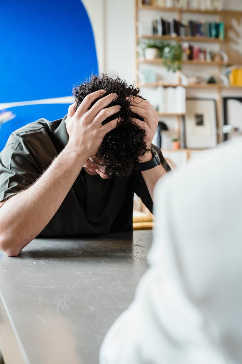 A person sitting at a table with their head on their hands.